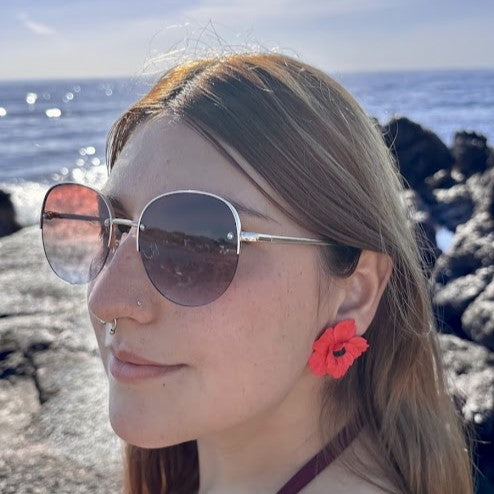 Modelo luciendo pendientes Poppy Soul de amapola en arcilla polimérica color rojo, talla M, con el mar de fondo
