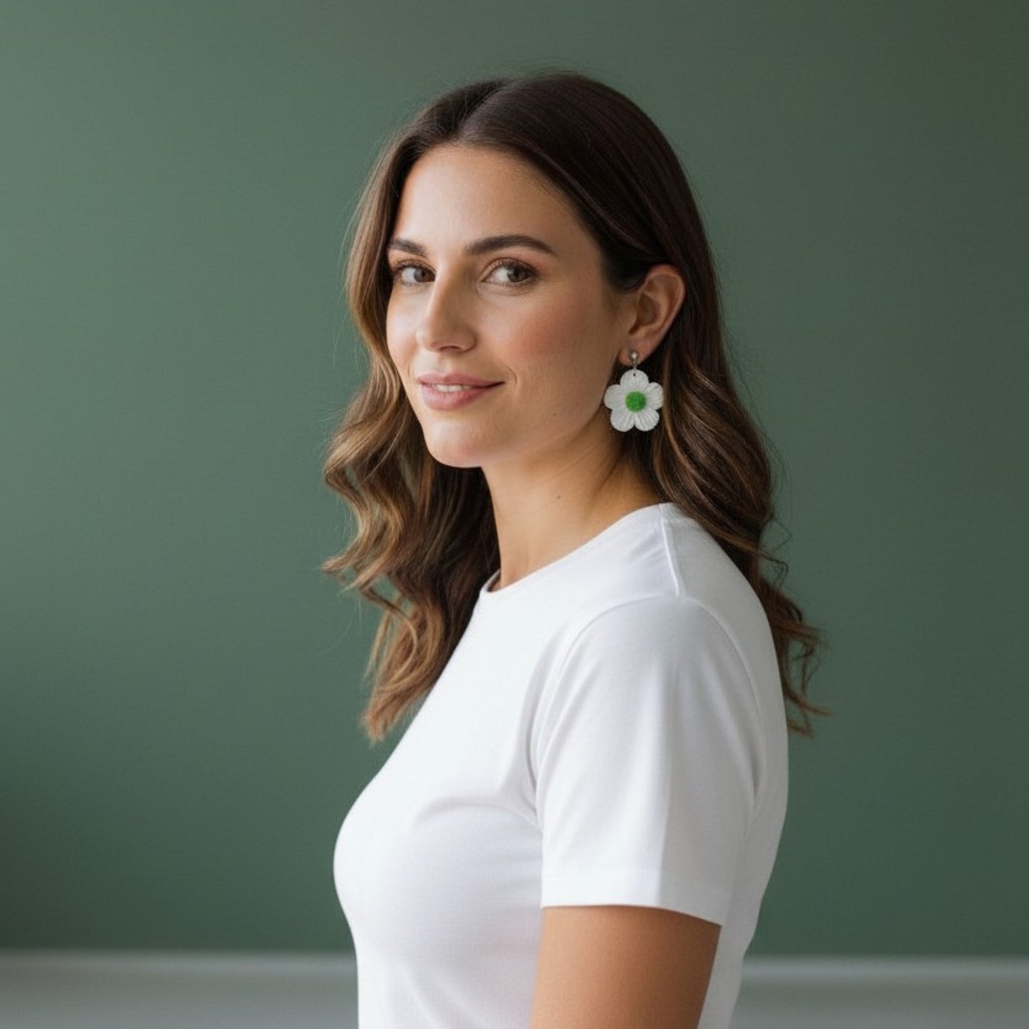 Mujer con cabello ondulado luciendo pendientes artesanales de margarita blanca y centro verde con camiseta blanca sobre fondo verde