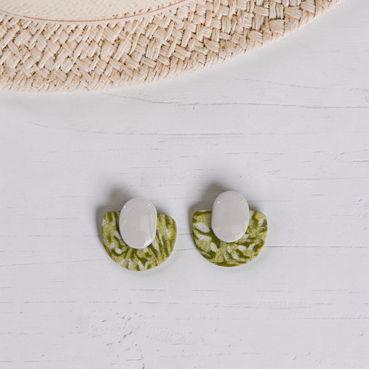 Pendientes Toffee verde y blanco de arcilla polimérica con textura, vista del par completo sobre fondo de madera blanca con sombrero de paja