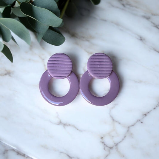 Pendientes artesanales de arcilla polimérica con forma circular en color malva, aro acabado con resina brillante UV, botón con textura de rayas y acabado mate