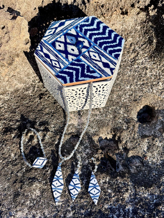 Conjunto de joyería artesanal Llengos Sal de arcilla polimérica en azul y blanco con diseño de rombos, presentado junto a la caja decorada de la colección Esencia Mallorquina de Pm_Art, sobre roca natural de Mallorca.
