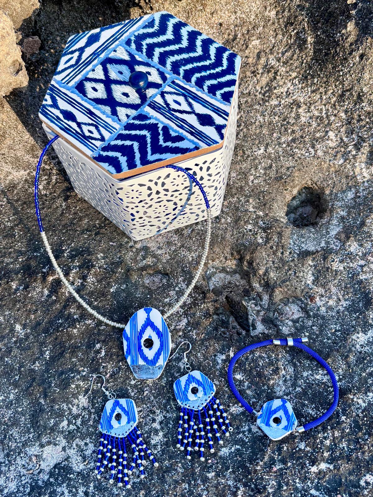 Conjunto de joyería artesanal con estampado de lenguas mallorquinas azules sobre roca natural costera. Incluye collar, pendientes largos y pulsera, junto a caja decorativa a juego de la colección Esencia Mallorquina.