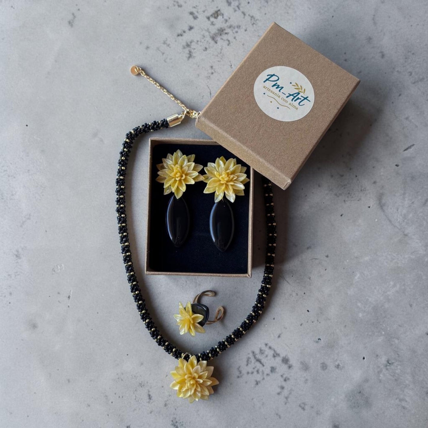 Conjunto de collar, pendientes y anillo: flores amarillas sobre base de arcilla negra con acabado en resina brillante y detalles dorados.