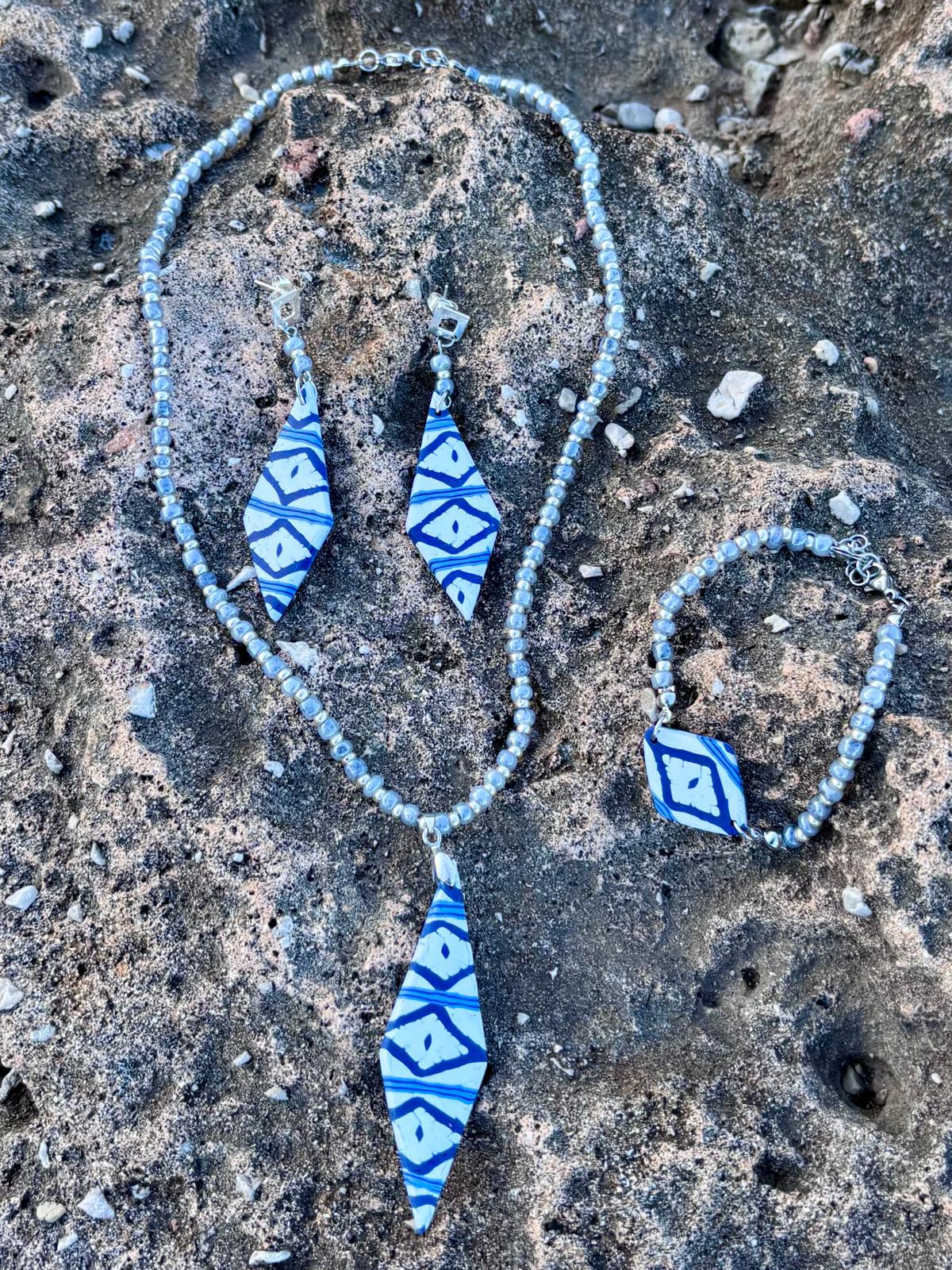 Conjunto completo Llengos Sal de arcilla polimérica en azul marino y blanco con cuentas de cristal en azul claro y plateado: collar con colgante rombo alargado, pendientes largos rombo y pulsera con pieza central rombo, sobre roca natural de Mallorca. Colección Esencia Mallorquina de Pm_Art.

