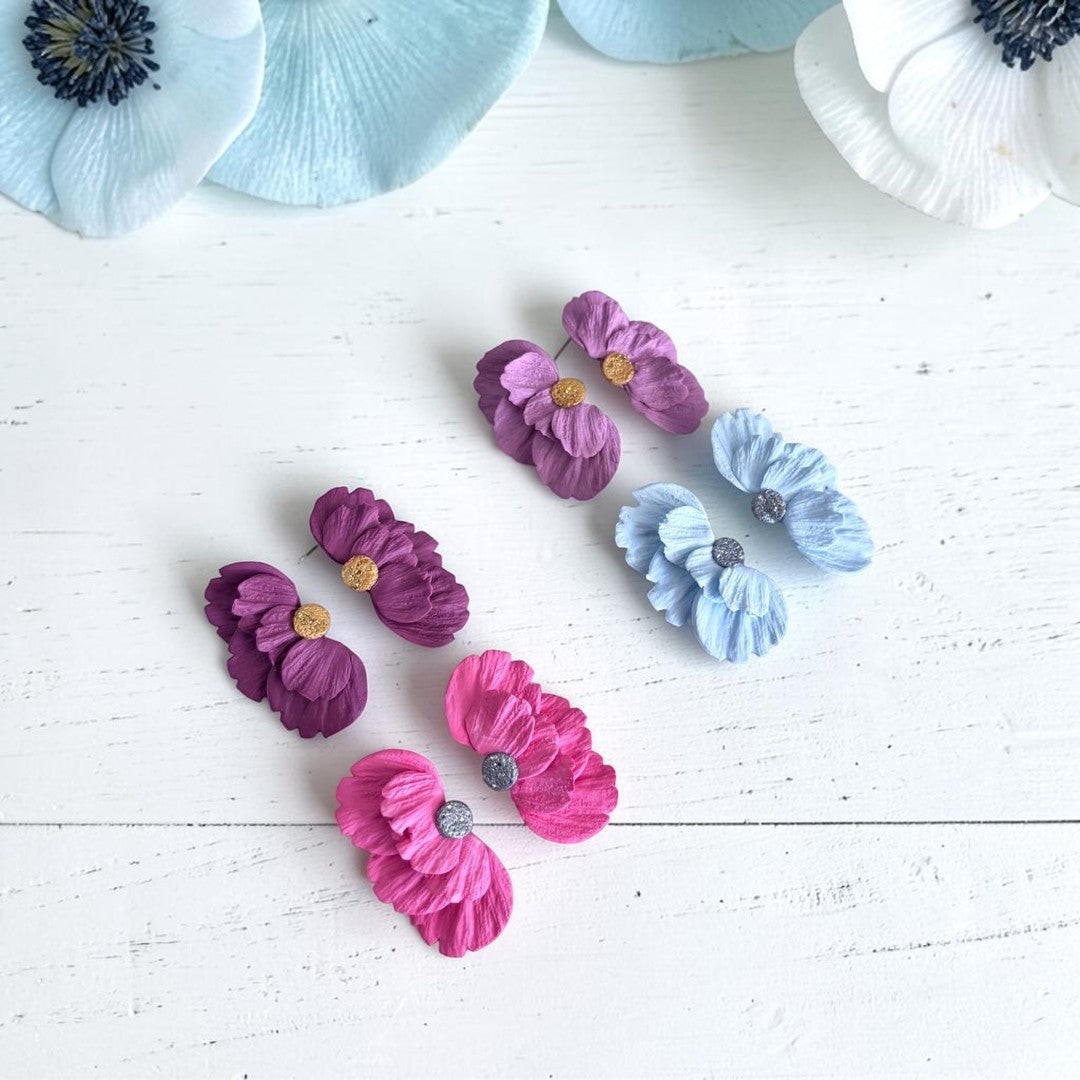 Pendientes artesanales Solleric de media flor en arcilla polimérica en varios colores, sobre madera blanca con flores naturales