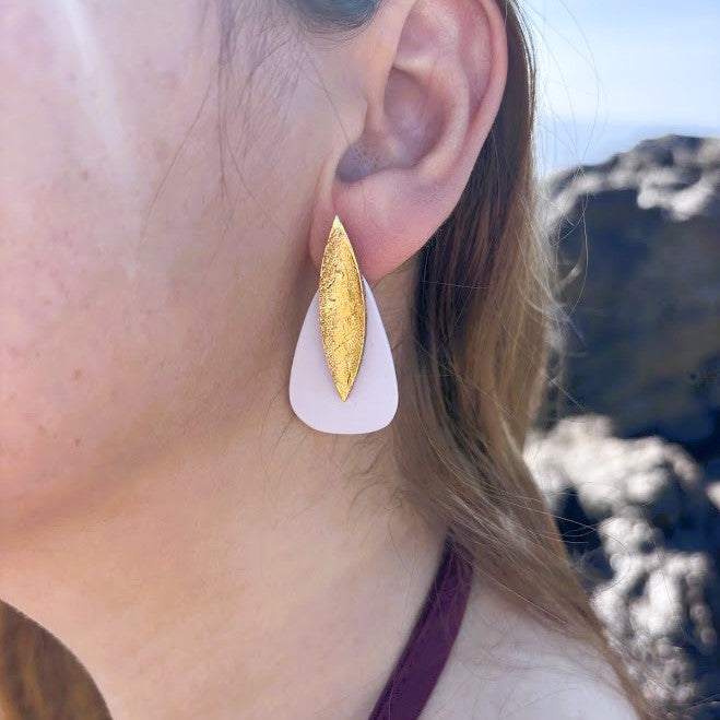 Modelo luciendo pendientes Sail color beig, plano de la oreja sobre fondo de rocas y mar