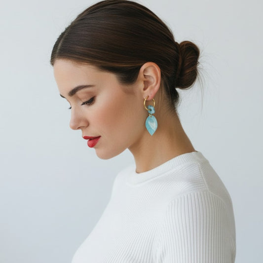 Mujer con moño luciendo pendientes artesanales Blue Leaf de arcilla polimérica azul turquesa y oro sobre jersey blanco