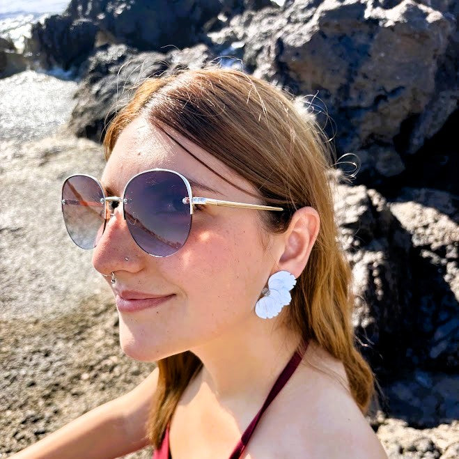 Modelo luciendo pendientes de media flor azul nube en arcilla polimérica junto al mar