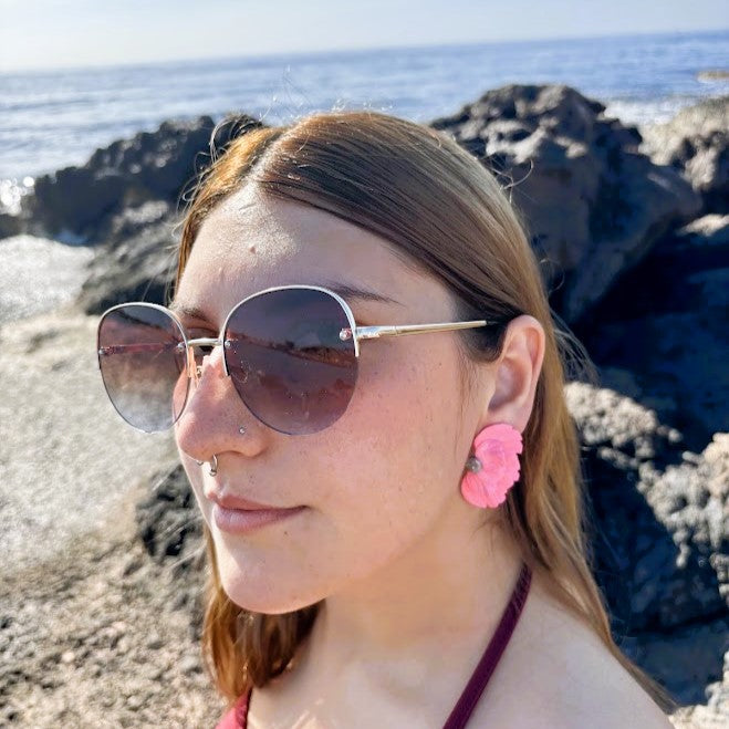 Modelo luciendo pendientes Solleric de media flor coral en arcilla polimérica frente al mar
