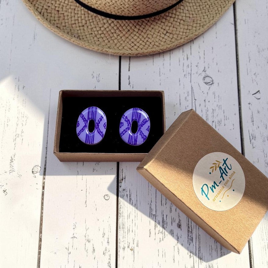 Pendientes botón Llengos Mar  lila en caja Pm-Art sobre fondo de madera blanca y sombrero de paja en la parte superior de la imagen