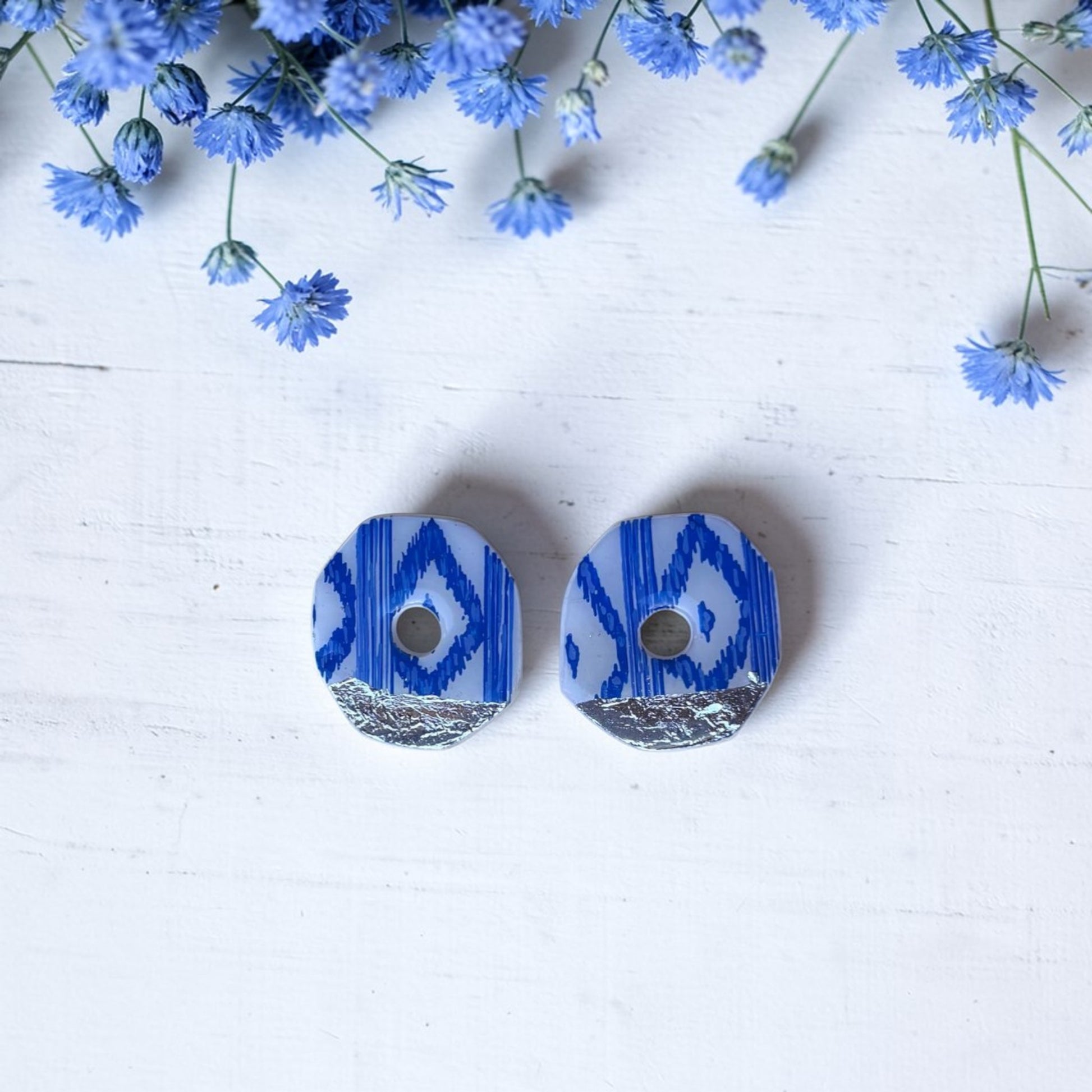 Pendientes de botón artesanales con estampado de lenguas mallorquinas azules y blancas. Formato geométrico de 3,5 cm sobre fondo blanco con flores decorativas.