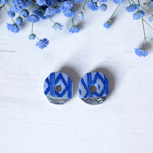 Pendientes de botón artesanales con estampado de lenguas mallorquinas azules y blancas. Formato geométrico de 3,5 cm sobre fondo blanco con flores decorativas.