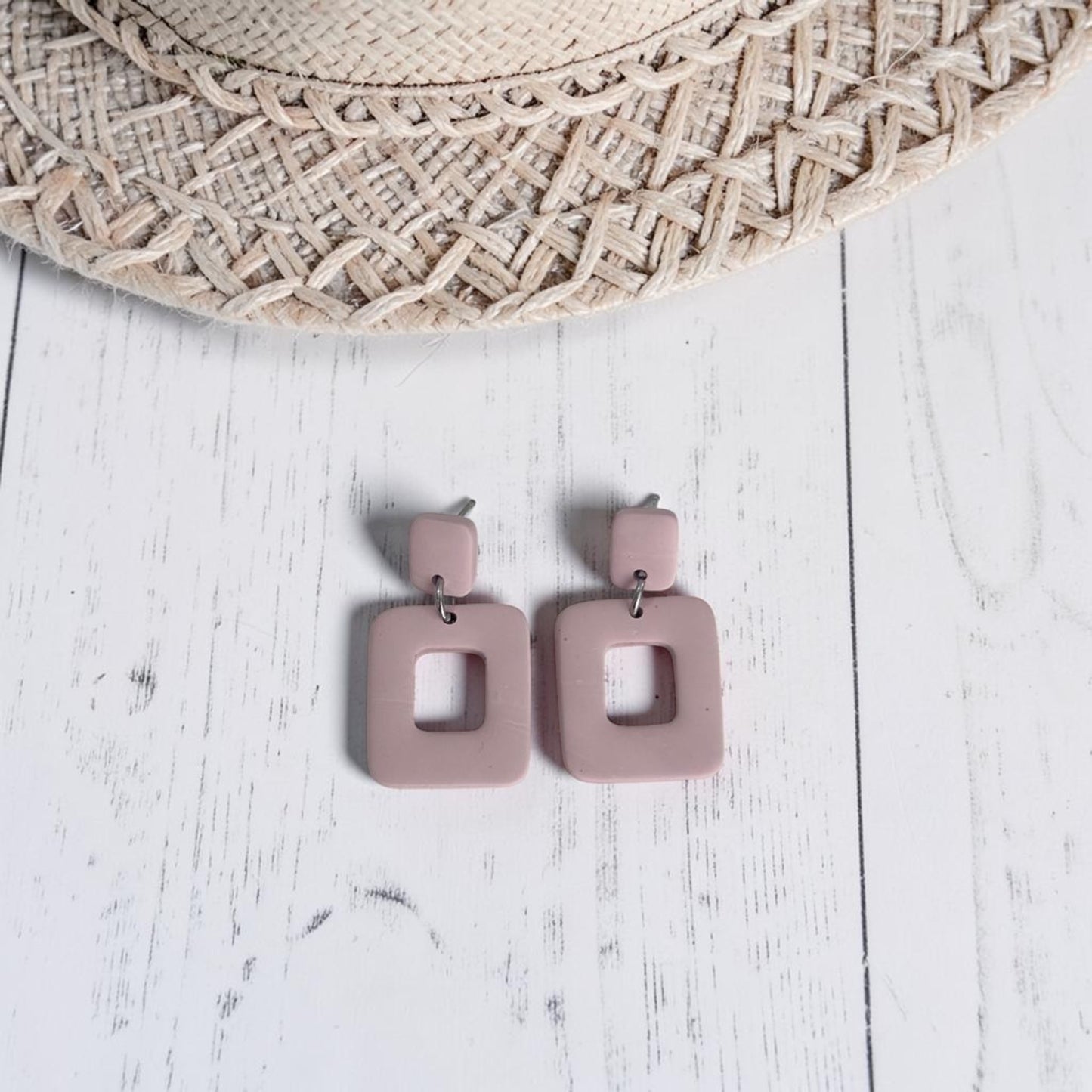 Pendientes Cubuk beige de arcilla polimérica, vista del par completo sobre fondo de madera blanca con sombrero de paja