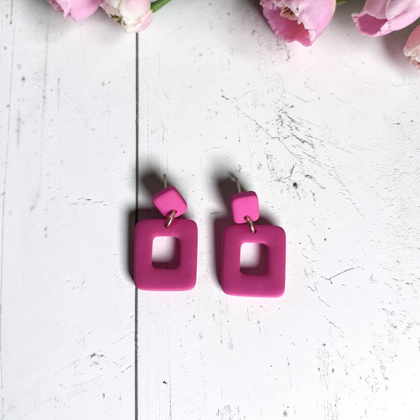 Pendientes Cubuk rosa coral de arcilla polimérica, vista del par completo sobre fondo de madera blanca con flores rosas
