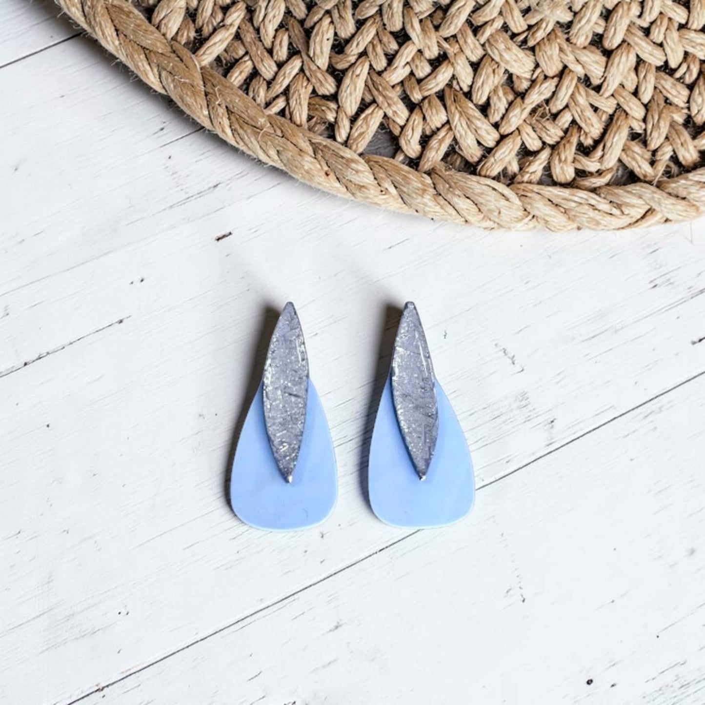 Pendientes artesanales Sail color azul nube de arcilla polimérica, diseño bohemio ligero, combinado con plata, sobre madera blanca y detalle de sombrero en la parte superior de la imagen