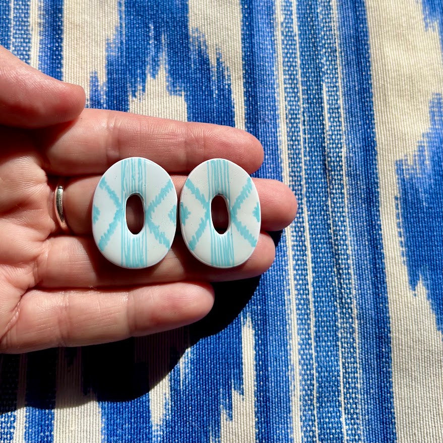 Primer plano de la mano sosteniendo los pendientes artesanales azul nube de la colección de lenguas mallorquinas pintados a mano