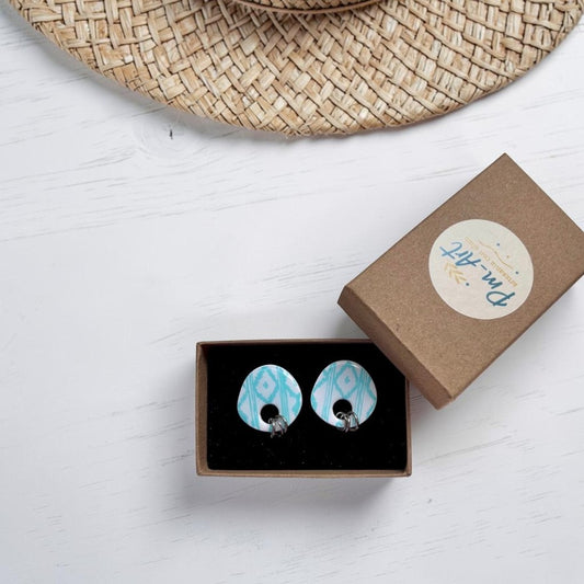 Pendientes de arcilla polimerica de boton color azul turquesa en caja de regalo Pm_Art sobre madera blanca y sombrero de paja en la parte superior