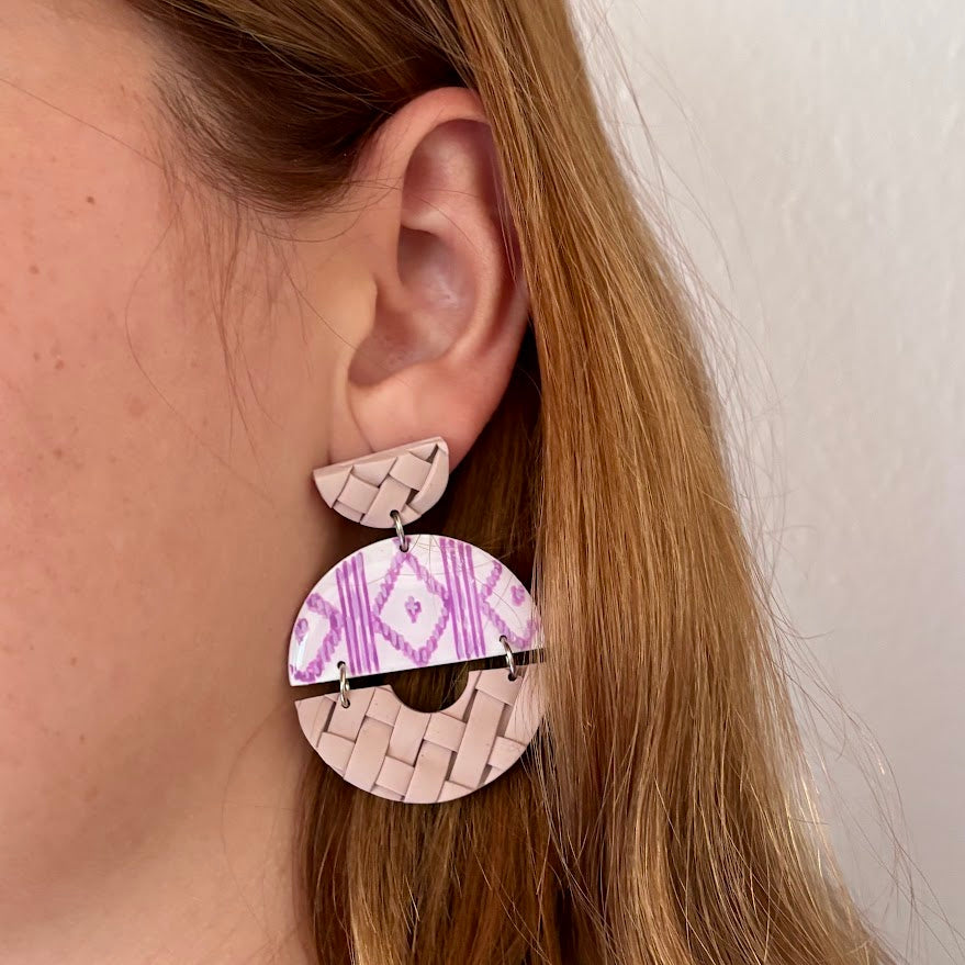Detalle en oreja de pendientes artesanales Arrels Alba de arcilla polimérica, estampado pintado a mano de llengos en lila y blanco con textura de llata en beige, colección Esencia Mallorquina