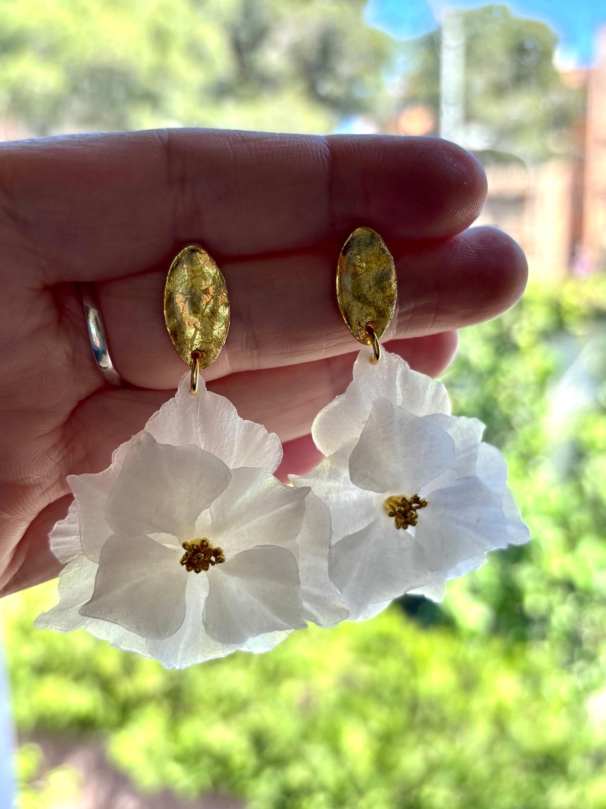 Pendientes de flor blanca artesanales con detalle dorado sostenidos en mano, joyería nupcial personalizable Mallorca
