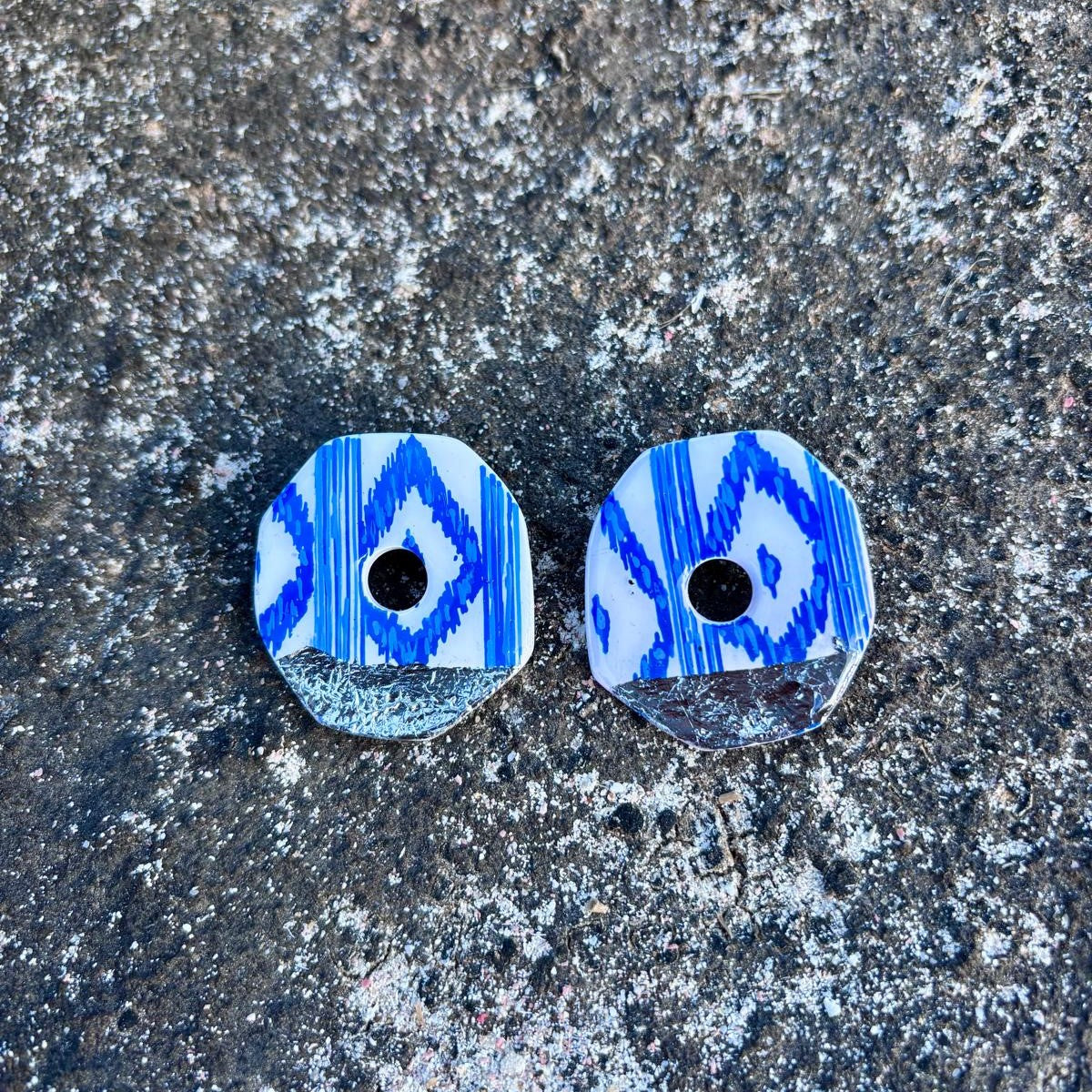 Pendientes de arcilla polimérica con diseño tradicional de Mallorca presentados sobre rocas costeras naturales.