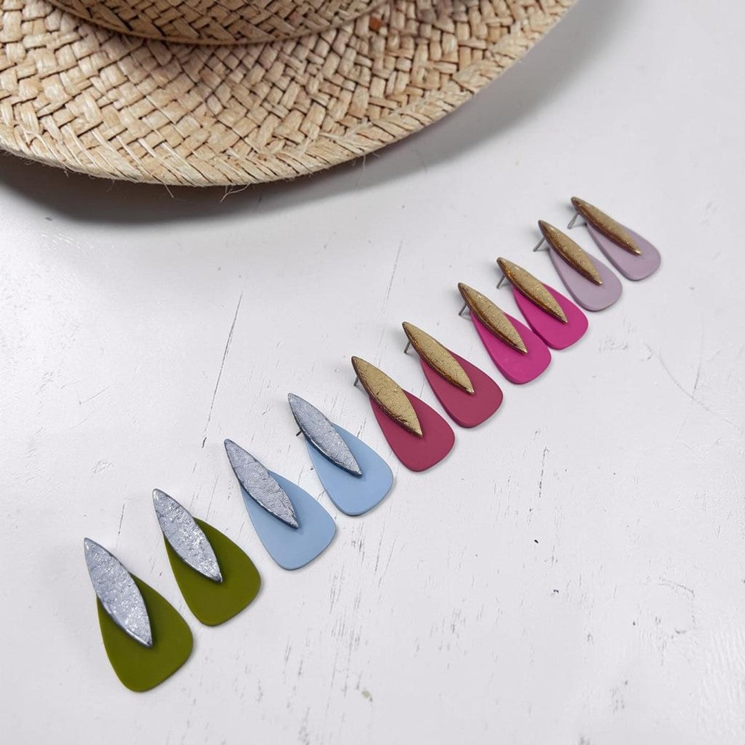 Pendientes artesanales modelo Sail de arcilla polimérica en varios colores: verde oliva, rosa coral, teja, azul nube, y beig sobre fondo  de madera rustica blanca con sombrero de paja
