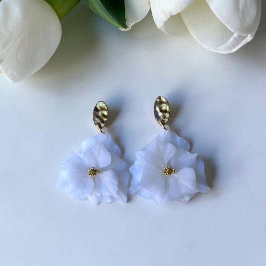 Pendientes florales artesanales blancos con base dorada, fotografiados junto a tulipán blanco - joyería nupcial Mallorca
