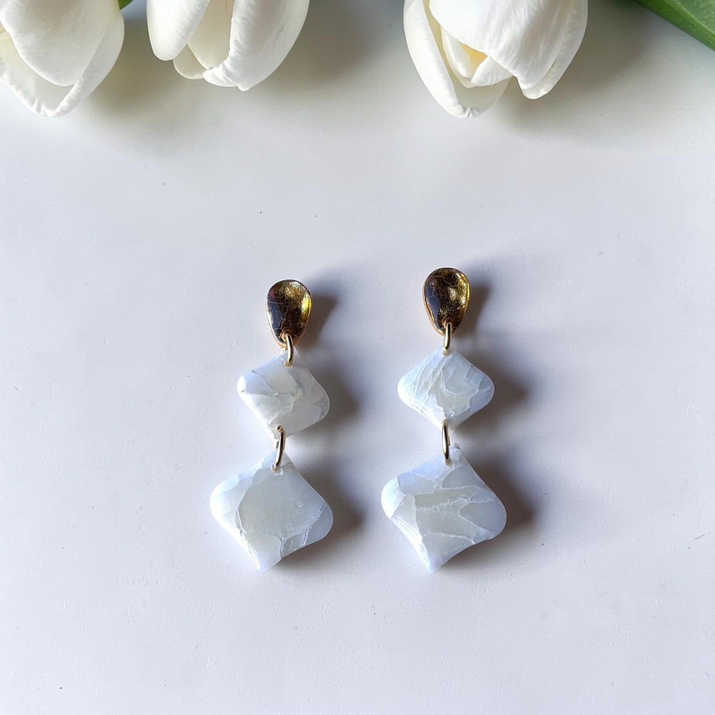 Pendientes geométricos artesanales Son Berga de arcilla polimérica efecto piedra blanca con enganche dorado, fotografiados con tulipanes blancos - joyería nupcial Mallorca
