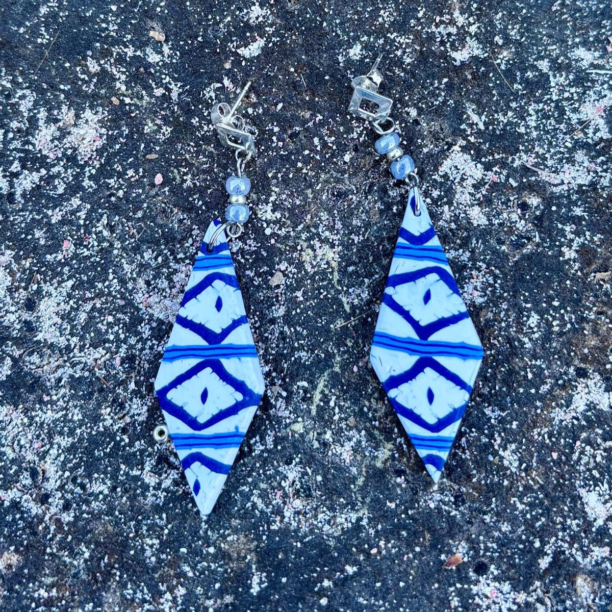 Pendientes largos artesanales Llengos Sal - Rombo largo de arcilla polimérica en azul marino y blanco con cuentas de vidrio celestes y fornitura bañada en plata, sobre roca oscura de Mallorca. Colección Esencia Mallorquina de Pm_Art.

