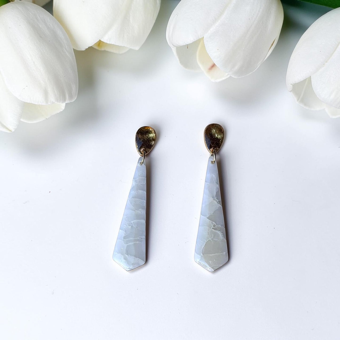 Pendientes largos artesanales Raixa de arcilla polimérica efecto piedra blanca con enganche dorado, fotografiados con tulipanes blancos - joyería nupcial Mallorca
