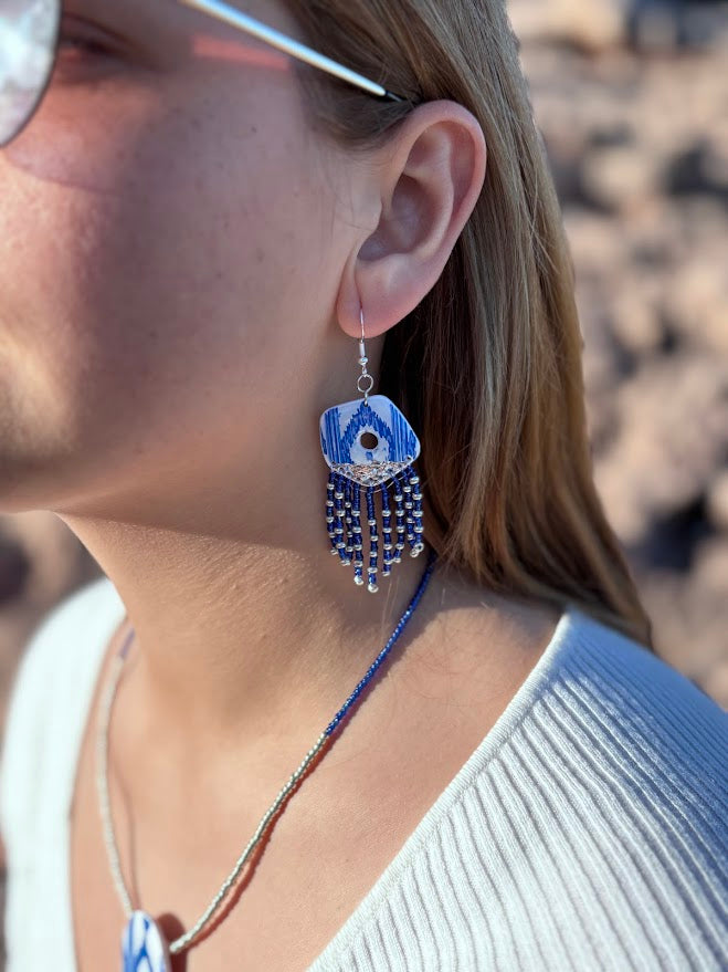 Primer plano de modelo luciendo pendientes largos de arcilla polimérica con flecos de cuentas. Se aprecia el detalle del diseño azul y blanco de la colección Esencia Mallorquina y cómo favorece el movimiento de la pieza puesta