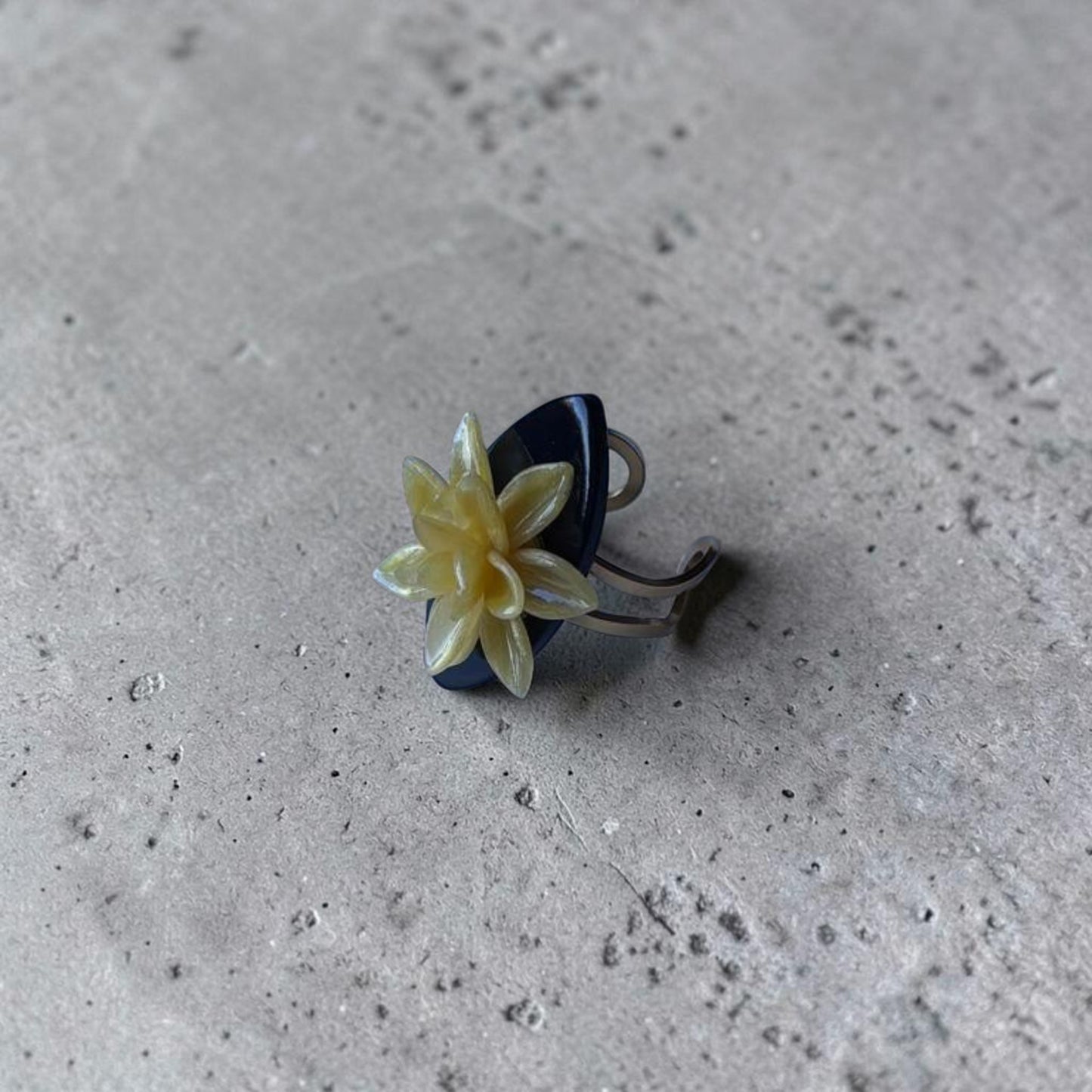 Anillo artesanal Modelo Galatzó con flor de dalia amarilla en arcilla polimérica sobre una base negra ovalada acabado en resina brillante y estructura ajustable