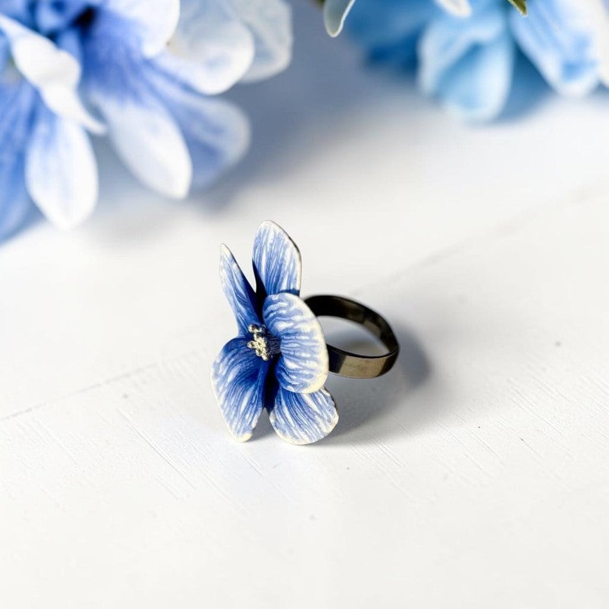 Vista lateral anillo flor de arcilla polimérica de color blanco y azul, base metálica de acero inoxidable color plata
