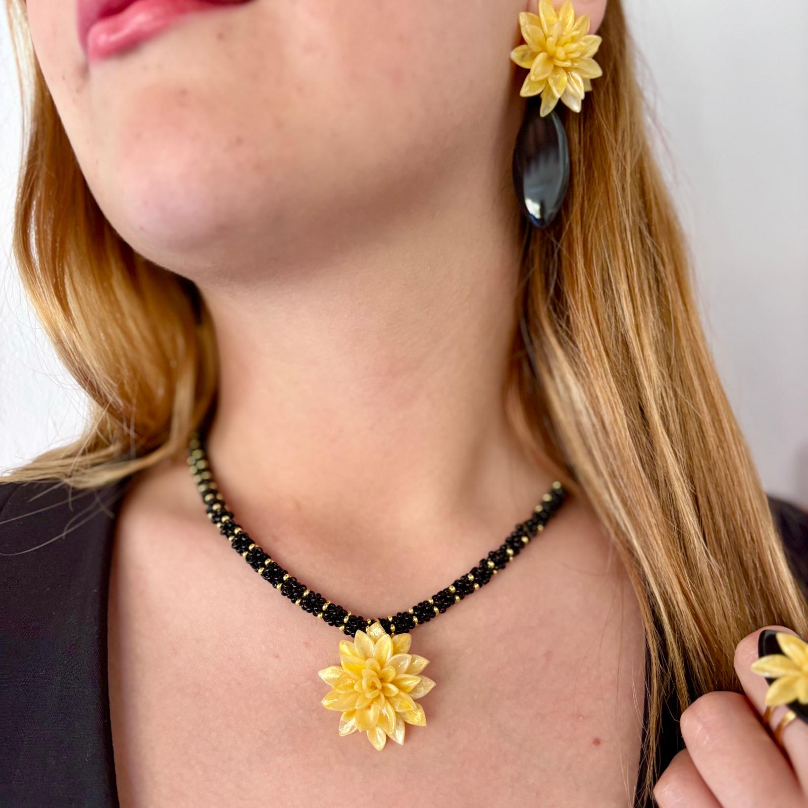 Primer plano de modelo con el collar Galatzó, destacando el cordón de cuentas de vidrio tejido a mano y el colgante floral amarillo.