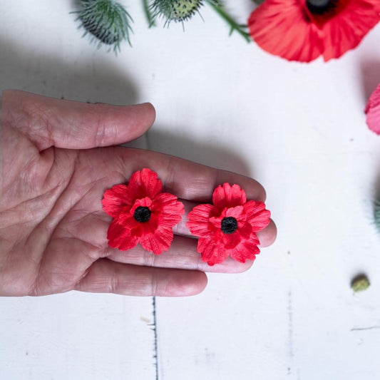 Pendientes artesanales de amapola en arcilla polimérica color rojo, sostenidos en la mano para mostrar el tamaño M