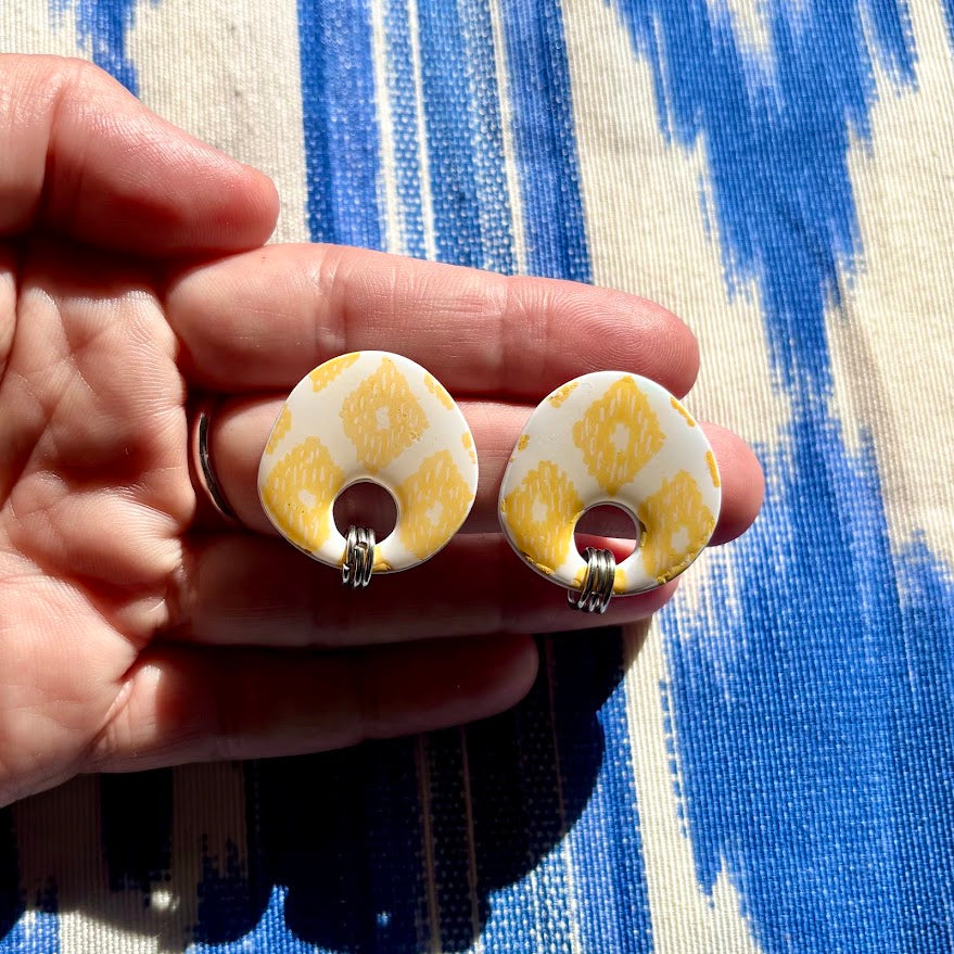 Pendientes llengos cel amarillos sostenidos en mano para apreciar su tamaño y acabado sobre tela de lenguas mallorquinas
