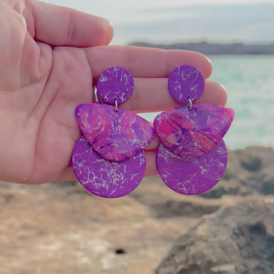 Video detalle de los pendientes artesanales Alfàbia en movimiento. Se muestra la ligereza y la textura de tres piezas en color púrpura: círculos con efecto craquelado plata y una pieza central marmoleada en tonos lila y amatista. Joyas de arcilla polimérica para invitadas de boda y eventos especiales en Mallorca