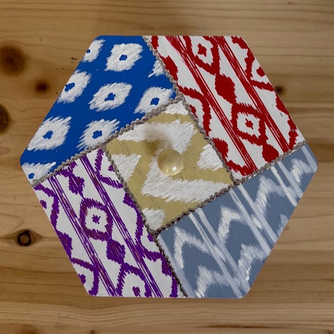 Primer plano de la tapa de madera de un joyero con patchwork pintado a mano que recrea el estampado típico de lenguas mallorquinas en varios colores.